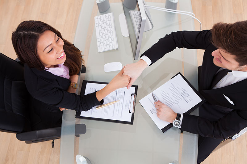 woman shaking hands with male sitting at desk